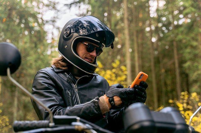 A man wearing a helmet is sitting on a motorcycle looking at his cell phone.
