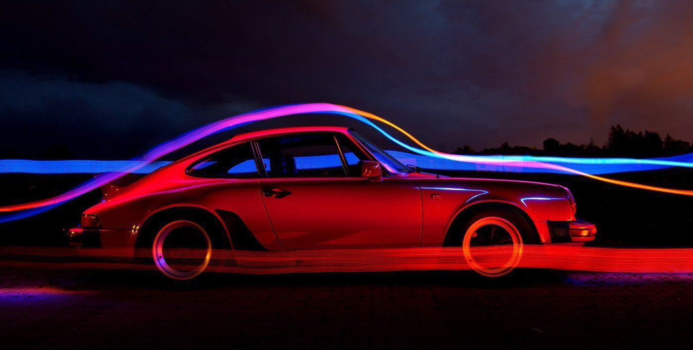 A red porsche is driving down a dark road at night.