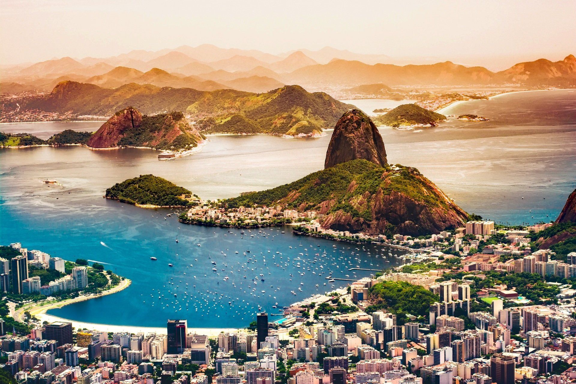 An aerial view of rio de janeiro with mountains in the background and a city in the foreground.
