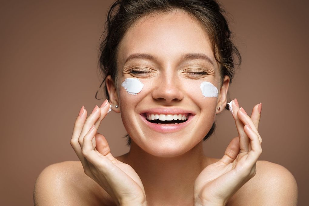 a woman is smiling while applying cream to her face