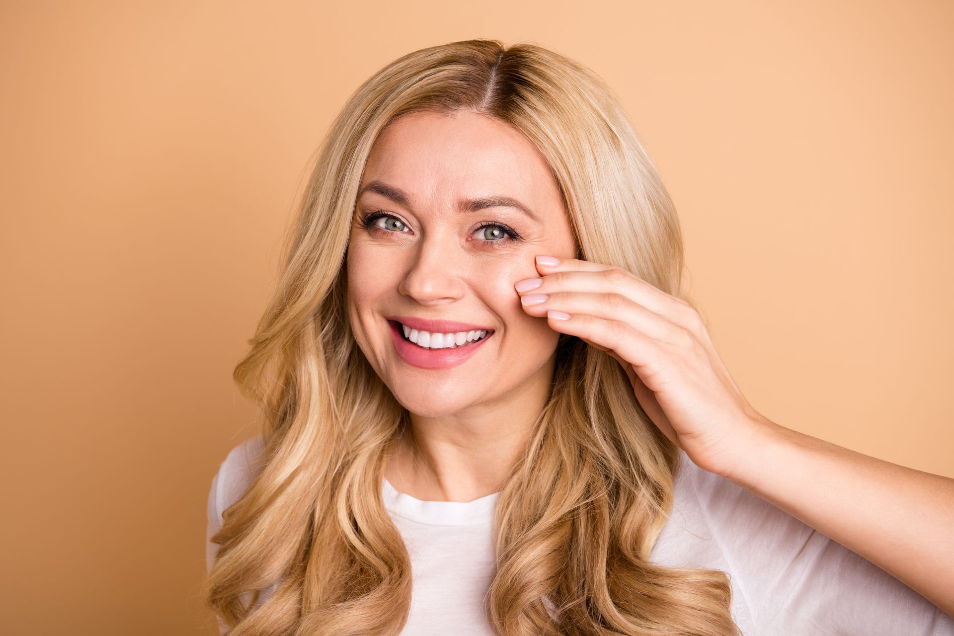 a woman with blonde hair is smiling and touching her face