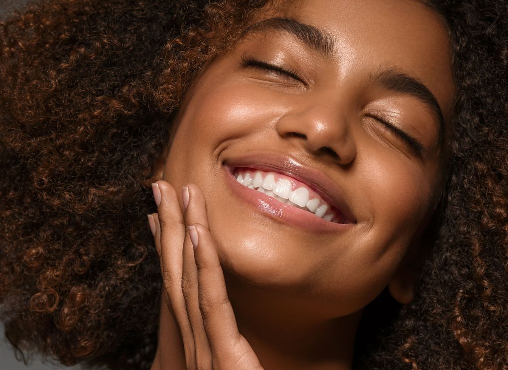 a woman with curly hair is smiling with her eyes closed