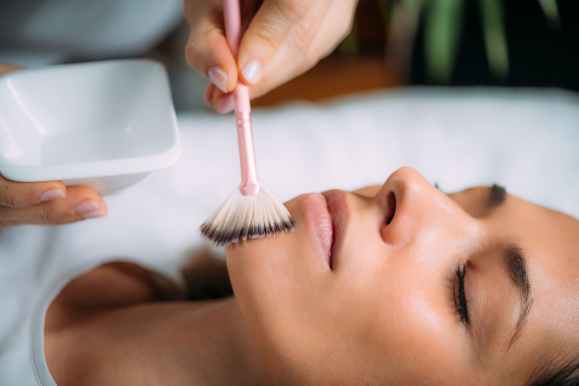 a woman is getting a facial treatment with a pink brush