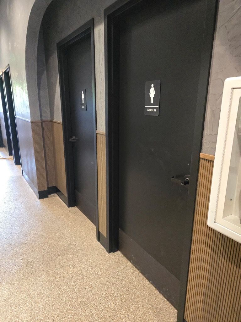 Hallway with two black restroom doors, one labeled with a gendered icon. Beige flooring.