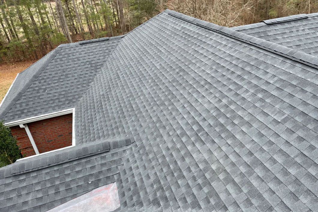 An aerial view of a gray roof of a house with trees in the background.