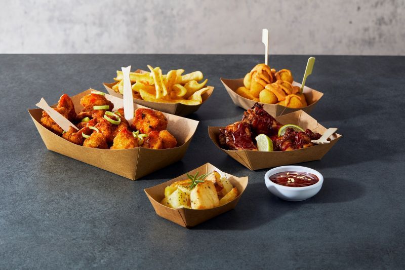 Assortimento di pollo fritto e patatine fritte in vassoi di carta con salse per intingere su un tavolo grigio.