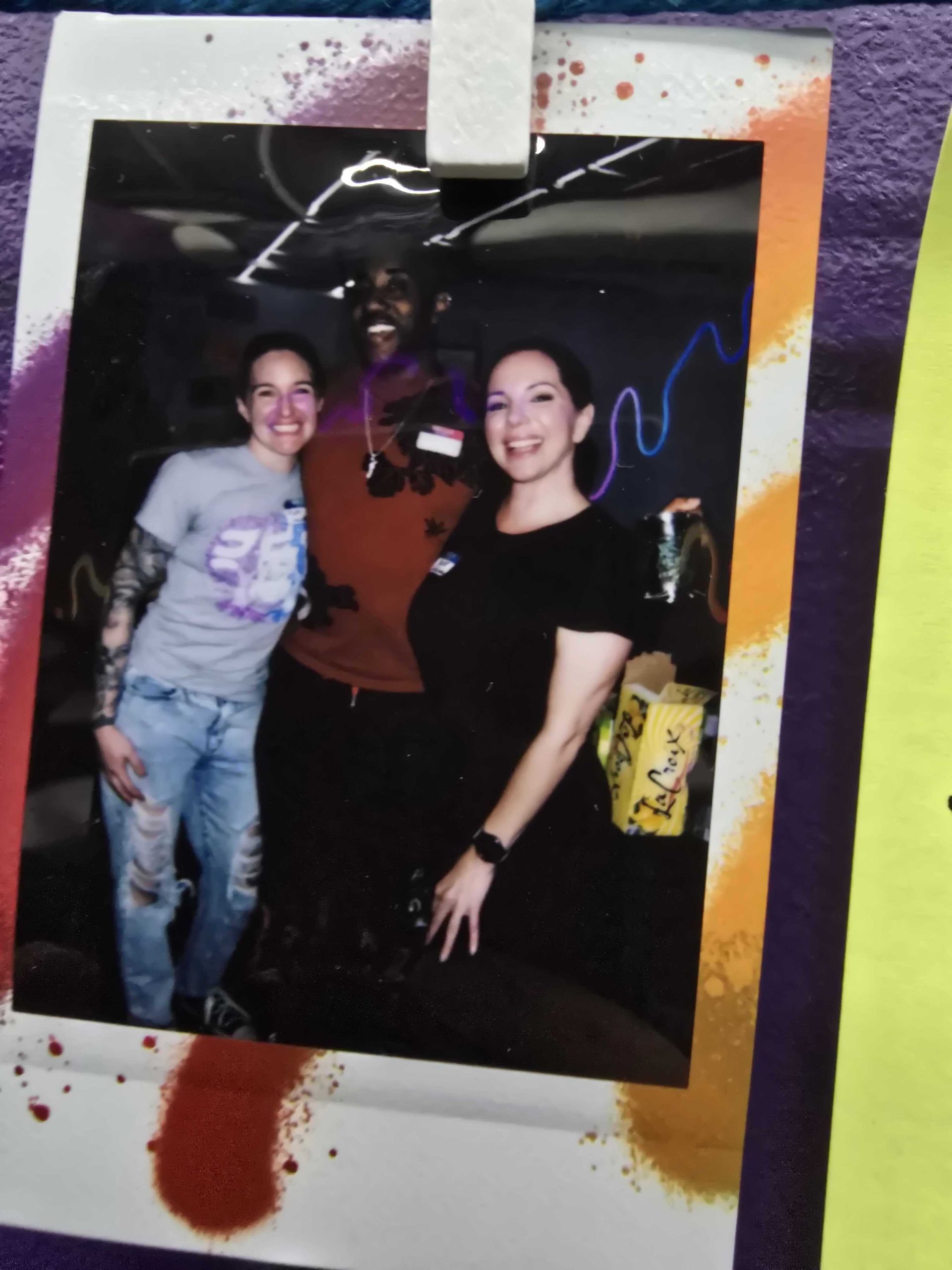 Three people smiling, posing for a photo. Person in the middle is wearing a red shirt. Others are wearing a black shirt and a gray shirt.