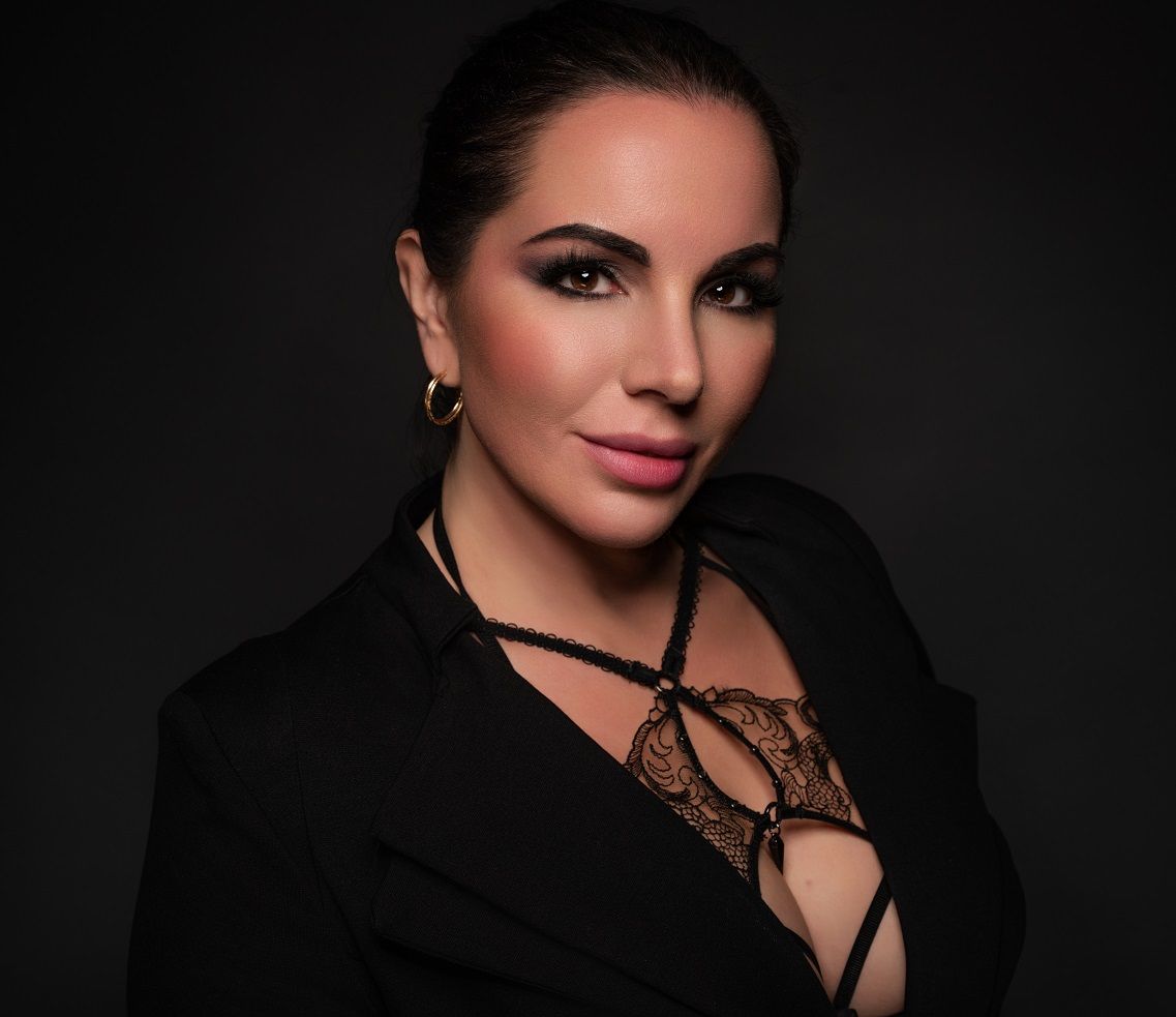 Goddess in black blazer with dark eye makeup, looking at the viewer.