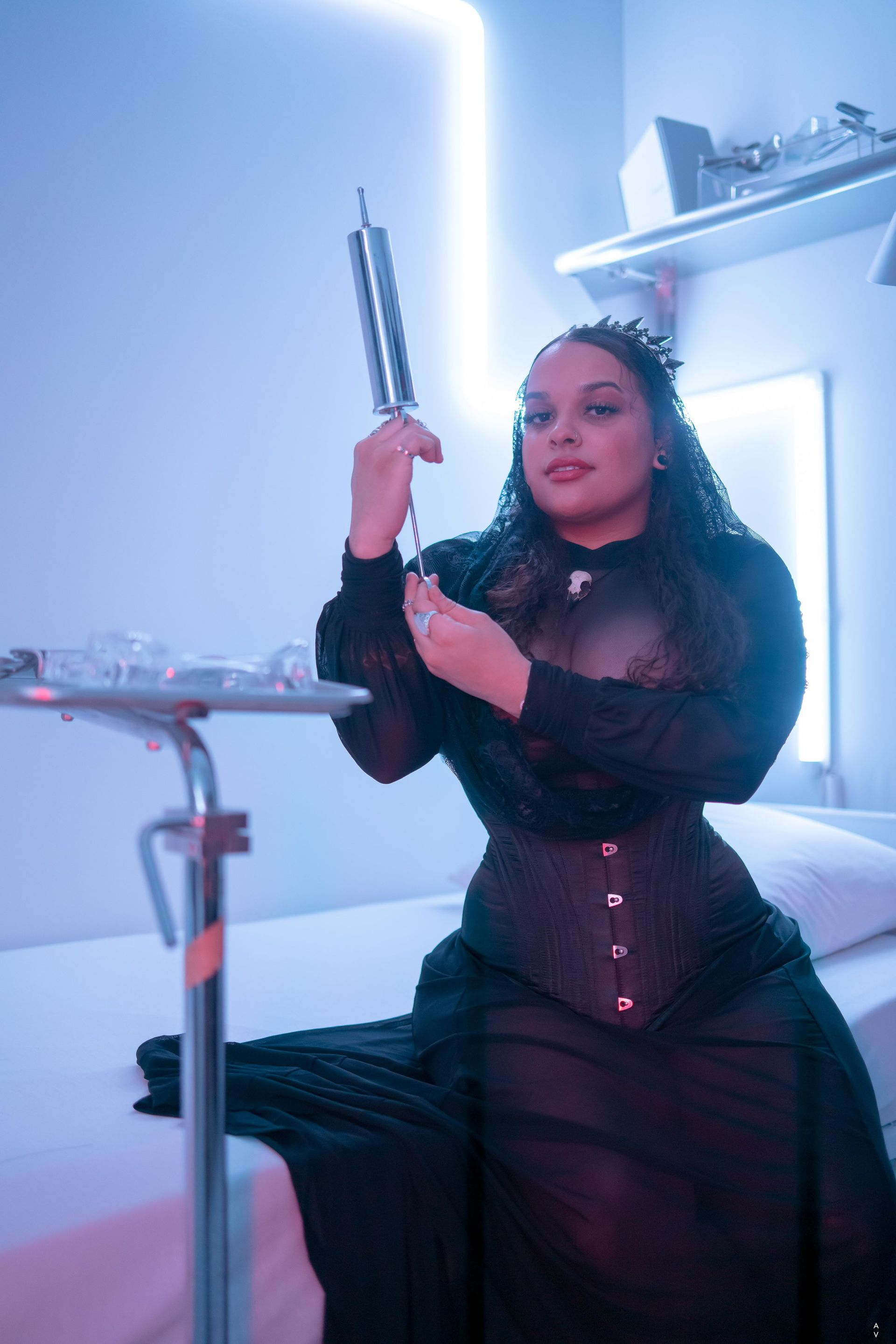 Woman in black dress and corset holds syringe in a futuristic, blue-lit setting.