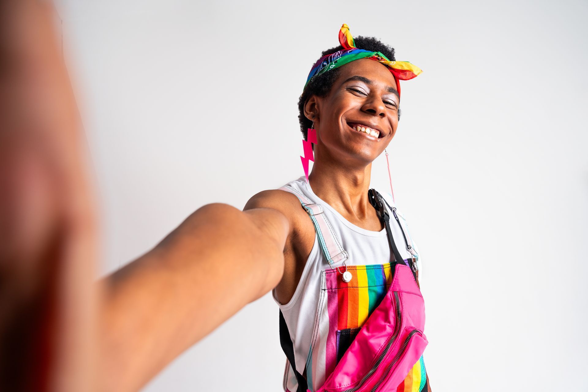 Person with rainbow accessories smiling, taking a selfie.
