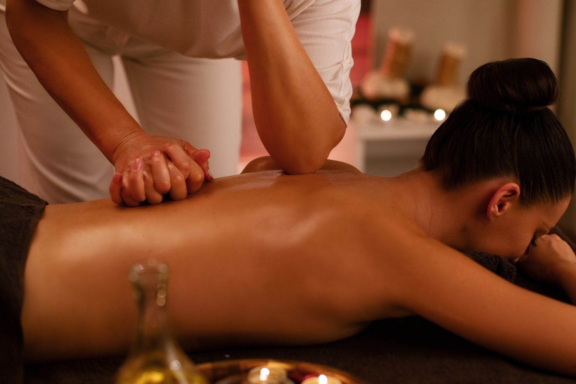 Spa massage with oil on a woman lying face down, therapist kneading her back in a warm, dim room