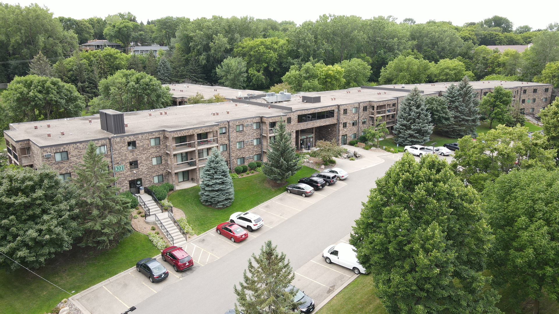 an aerial view of a large apartment building with cars parked in front of it surrounded by trees .