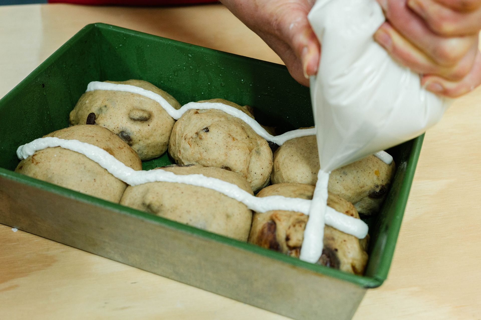 piping cross onto hot cross buns in pan