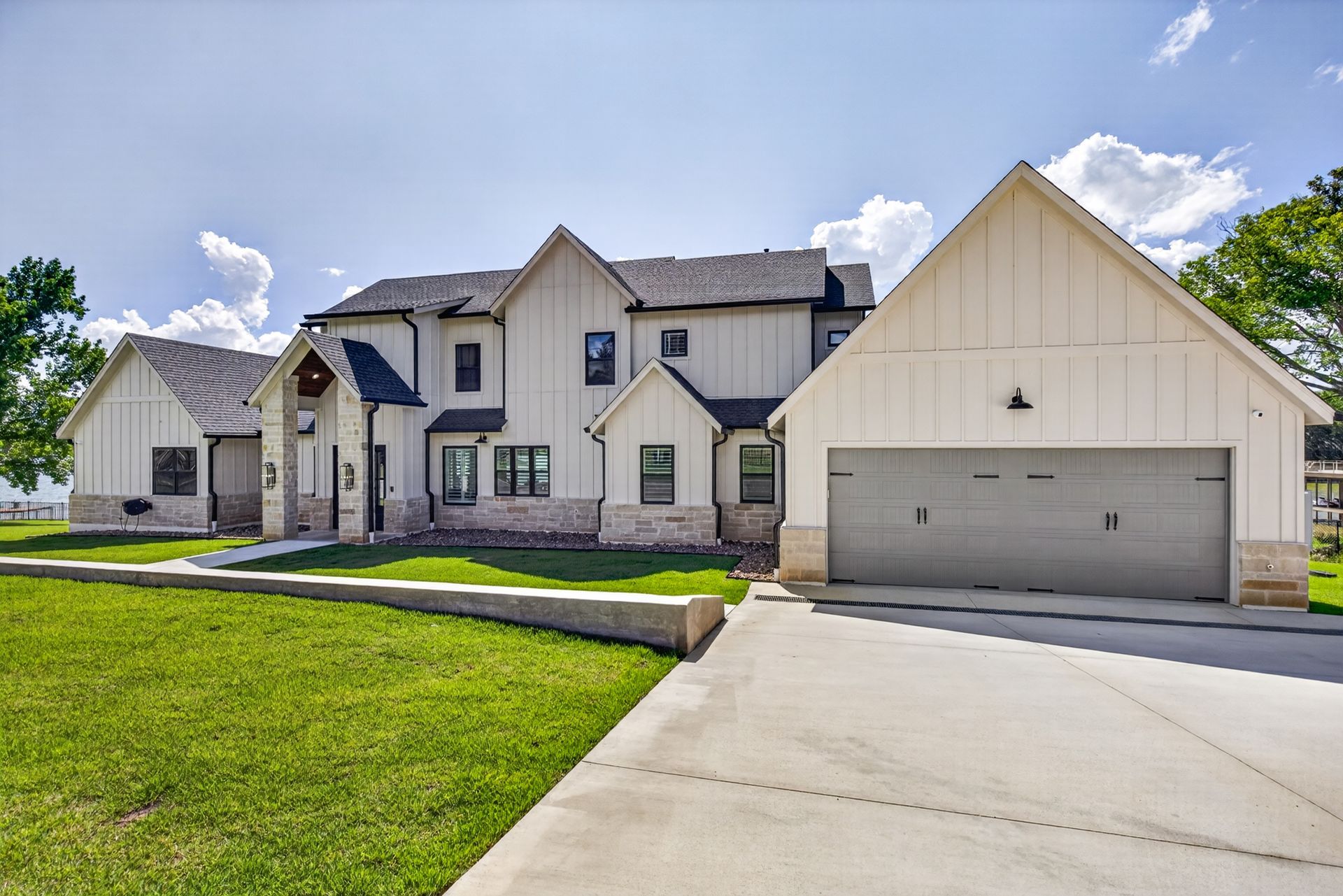 Modern two-story suburban house with white siding, black shutters, and a two-car garage under a bright blue sky