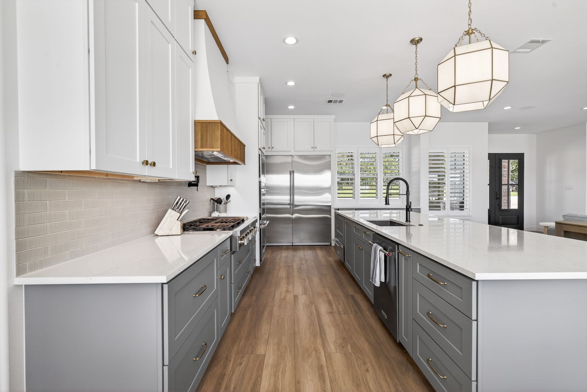 Bright modern kitchen with white cabinets, gray island, stainless steel appliances, and wood floors