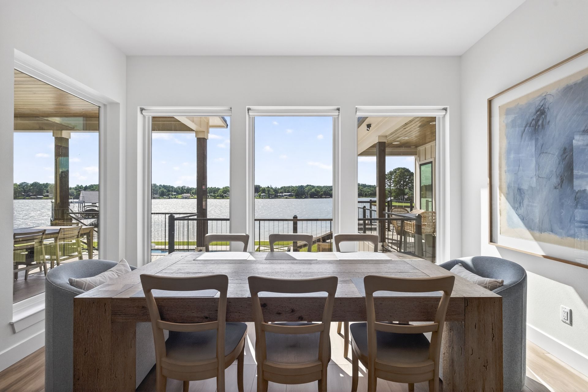Dining room with a wooden table and chairs overlooking a bright waterfront view through large windows