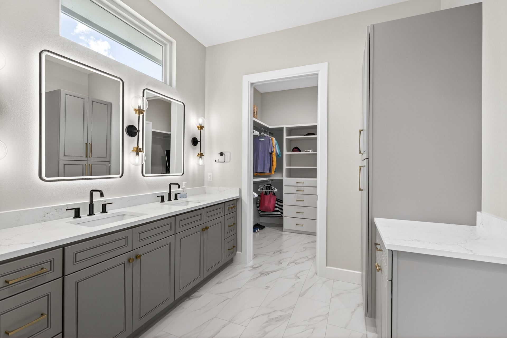 Modern bathroom with double vanity, mirrors, white marble floor, and open walk-in closet door