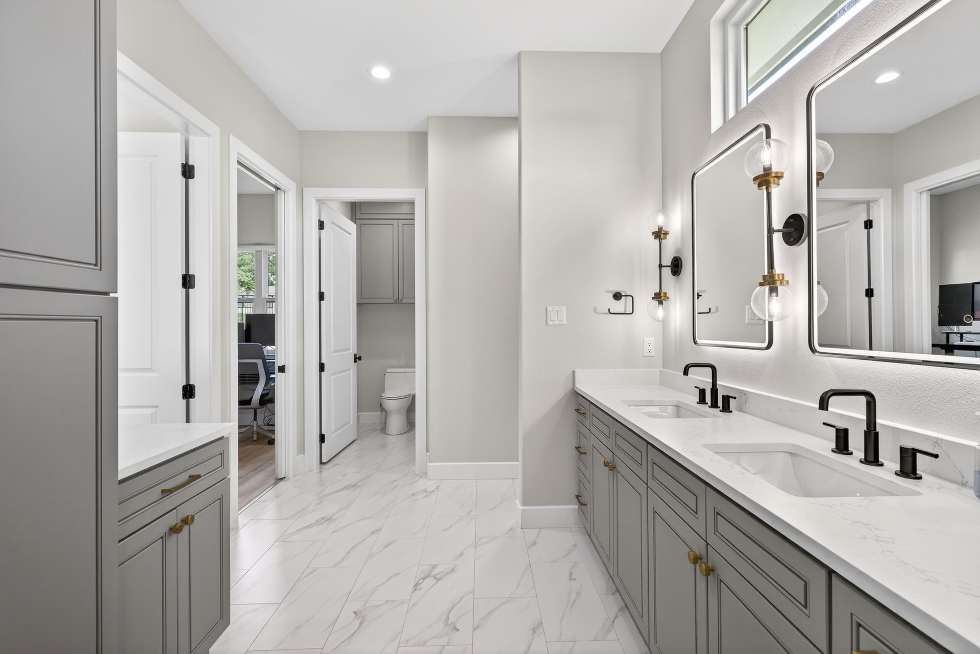 Bright modern bathroom with gray cabinets, white marble counters, and large mirrors