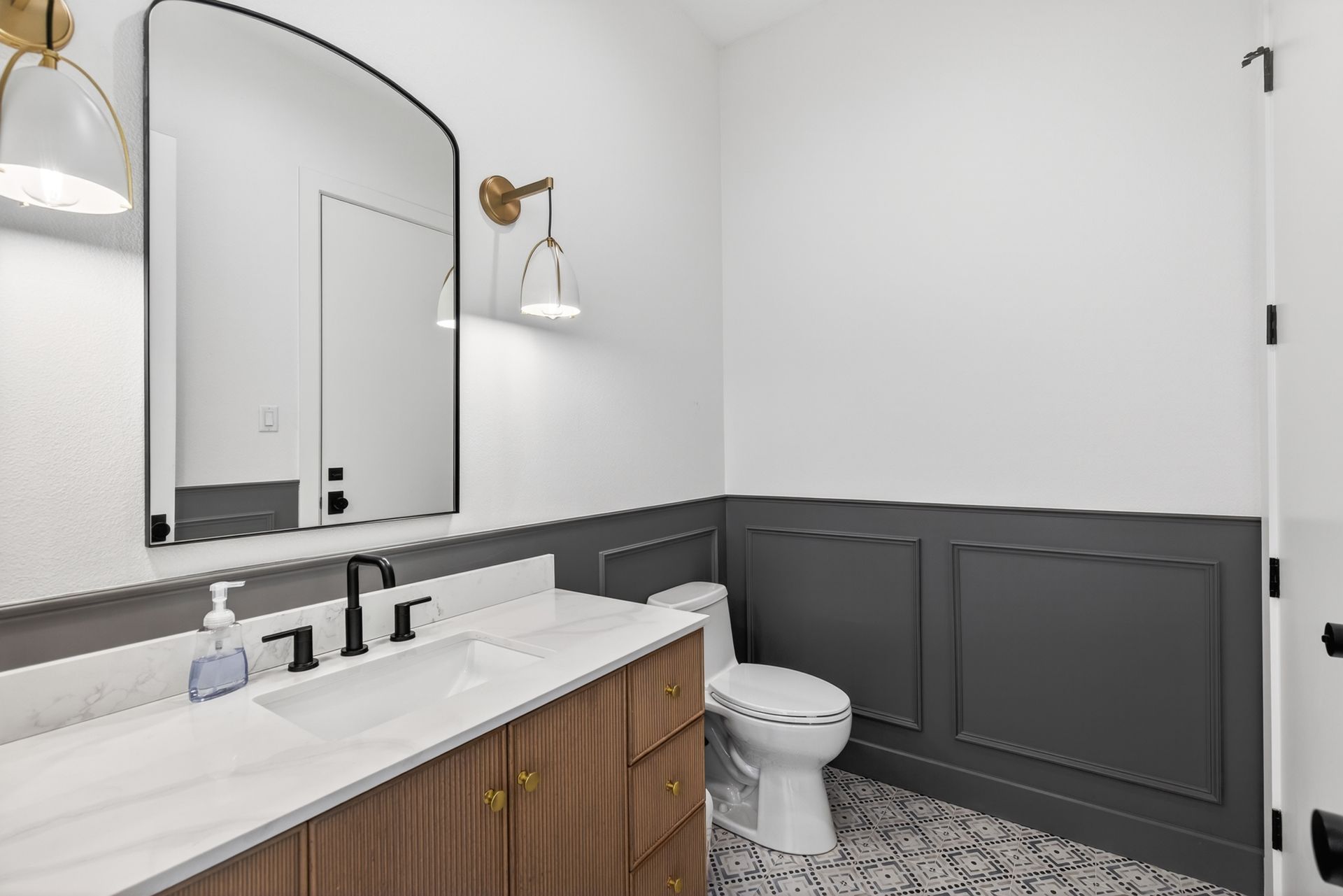 Modern bathroom with white walls, dark gray wainscoting, wood vanity, and a patterned tile floor