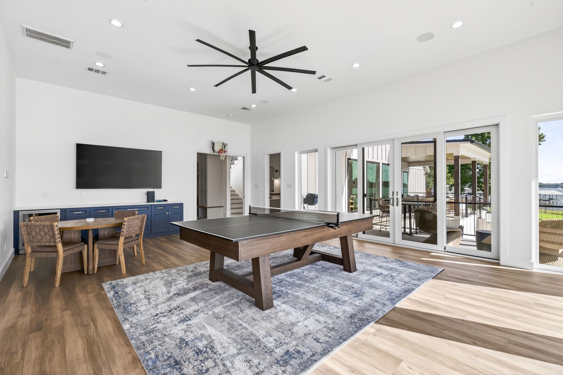 Bright modern living room with pool table, large TV, wood floors, and sliding glass doors to patio