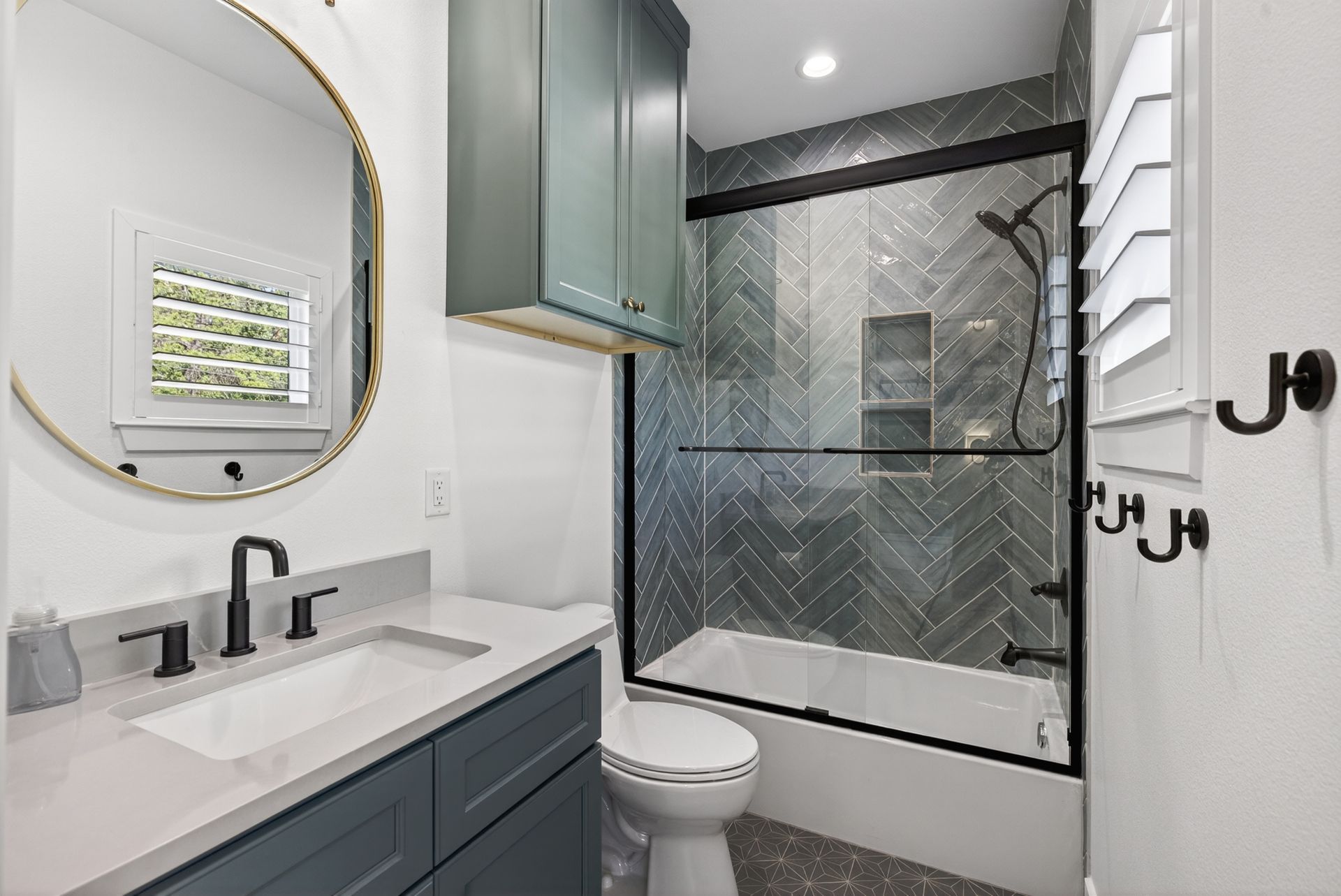 Modern bathroom with blue vanity, round mirror, toilet, and black-framed glass shower.