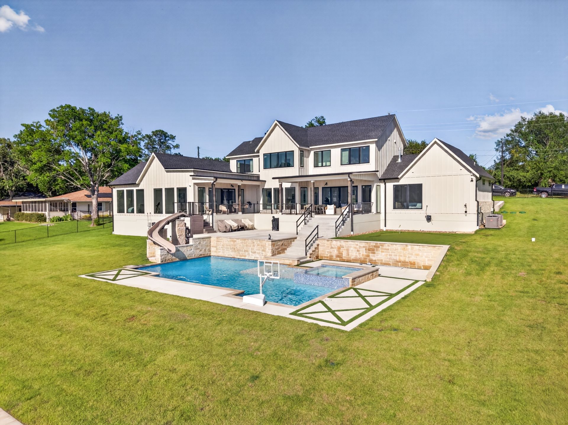 Large white house with a backyard pool, patio seating, and a green lawn on a sunny day