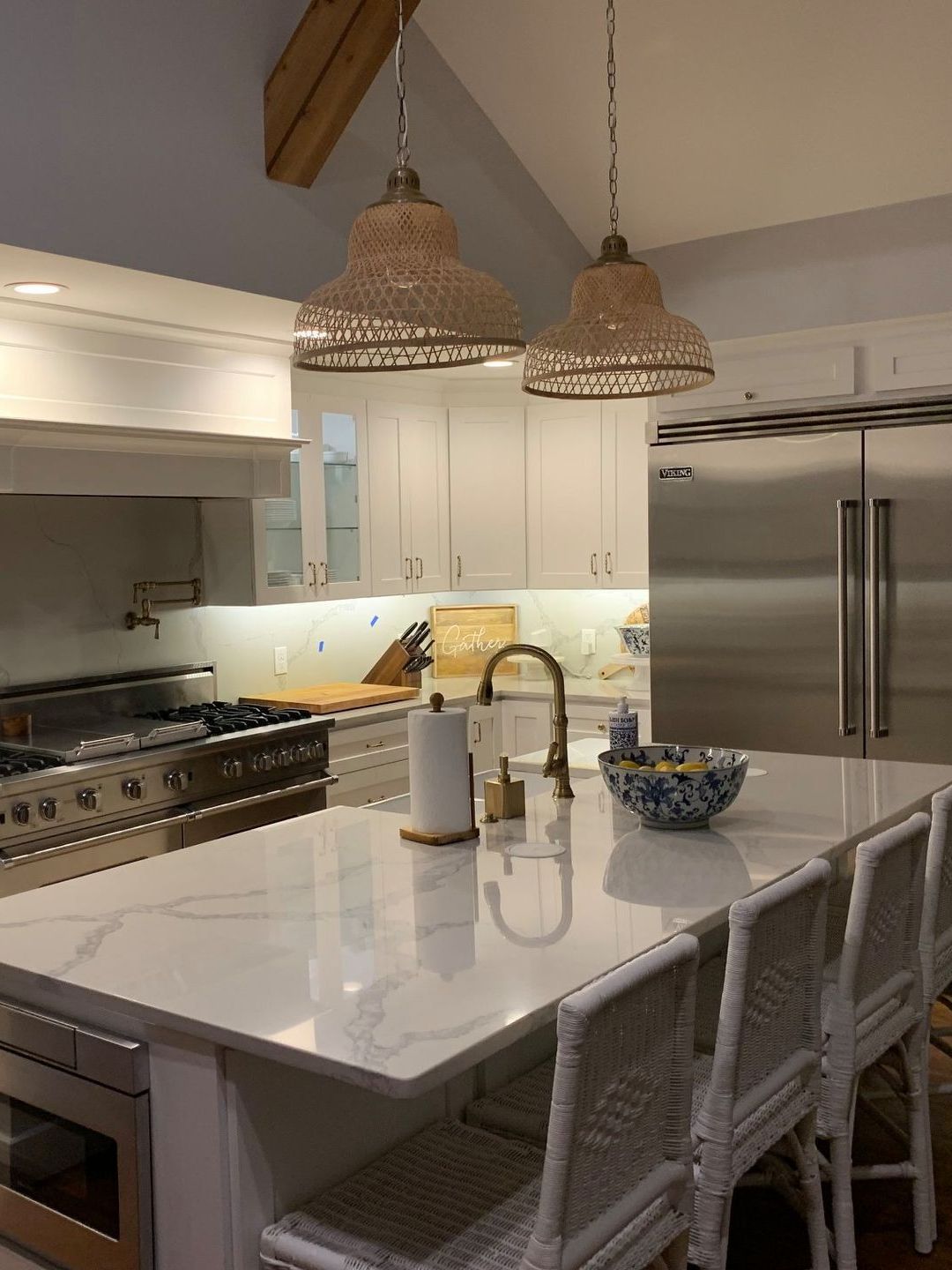 A kitchen with white cabinets , stainless steel appliances , a large island , and wicker chairs.