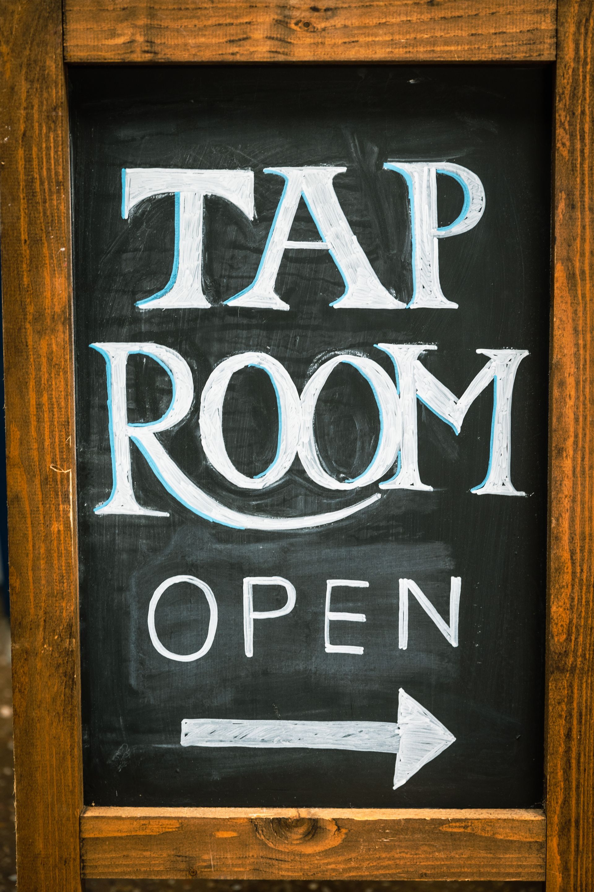 A chalkboard sign that says tap room open with an arrow pointing to the right.