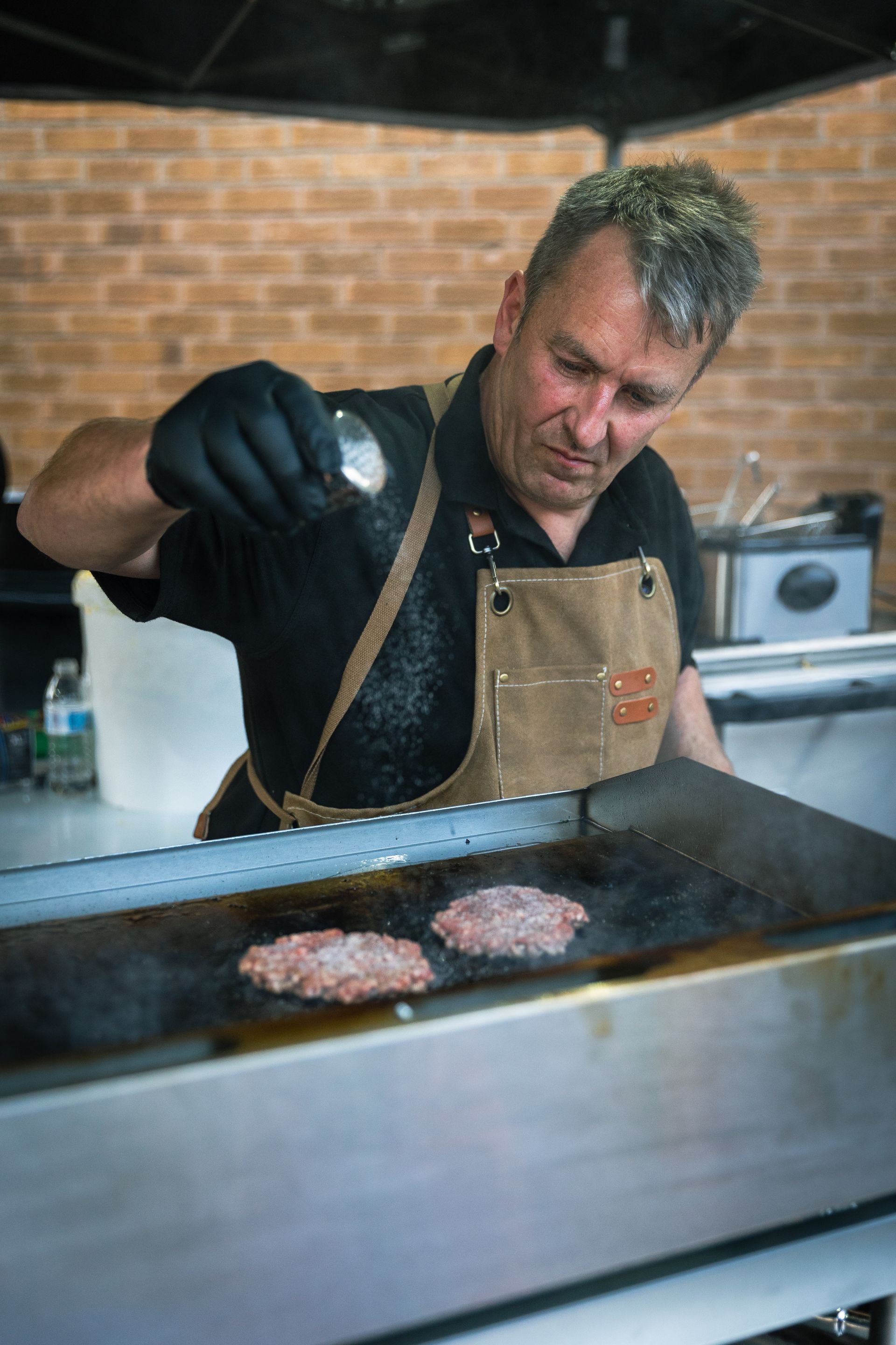 A man is cooking hamburgers on a grill in a kitchen.