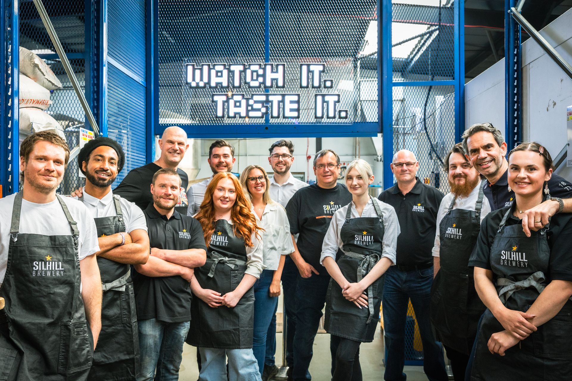 A group of people standing in front of a sign that says watch it taste it