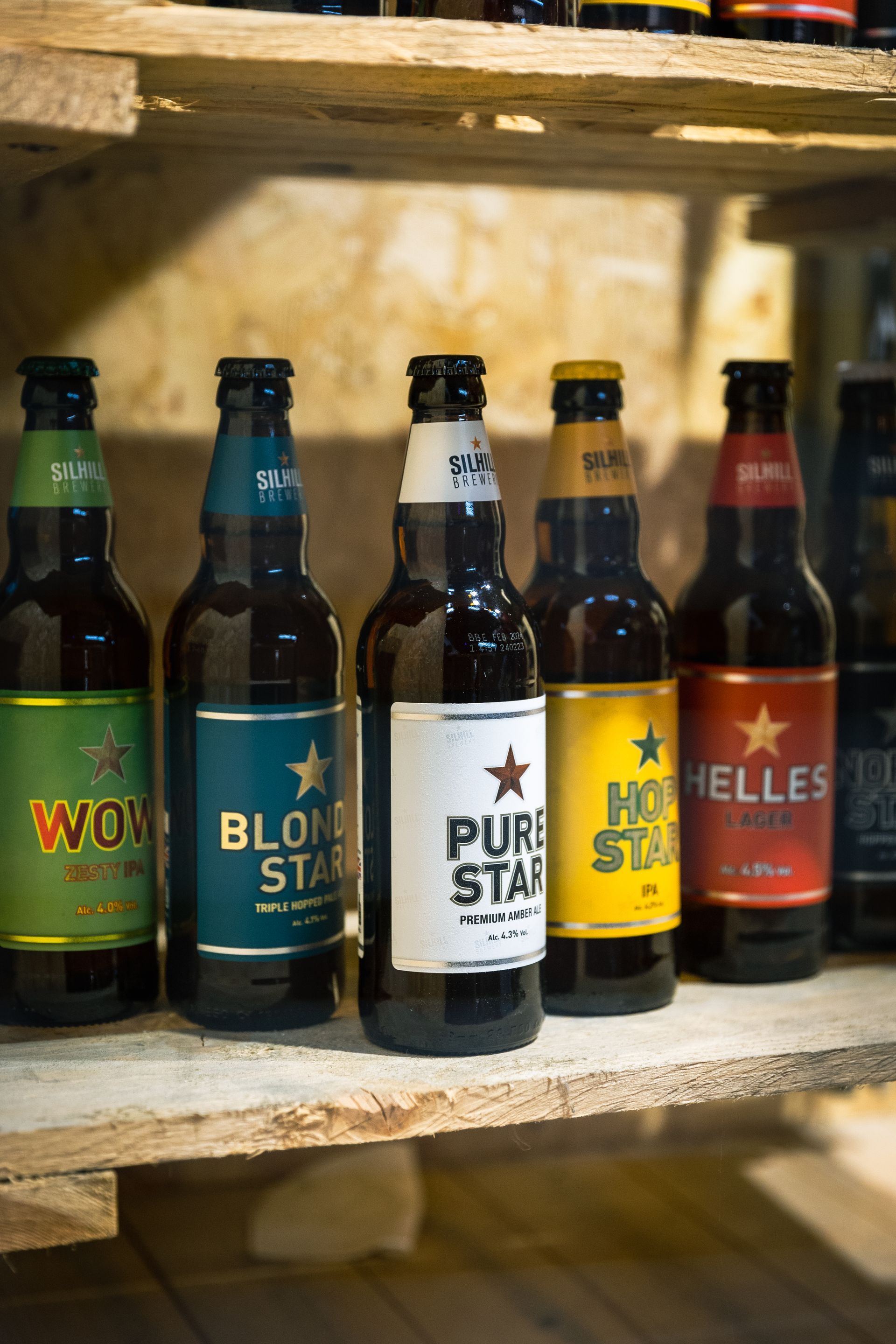 Several bottles of beer are lined up on a wooden shelf