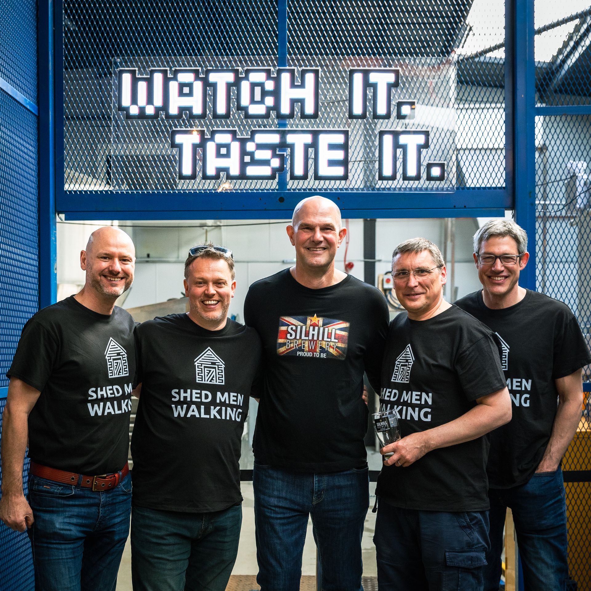 A group of men standing in front of a sign that says watch it taste it