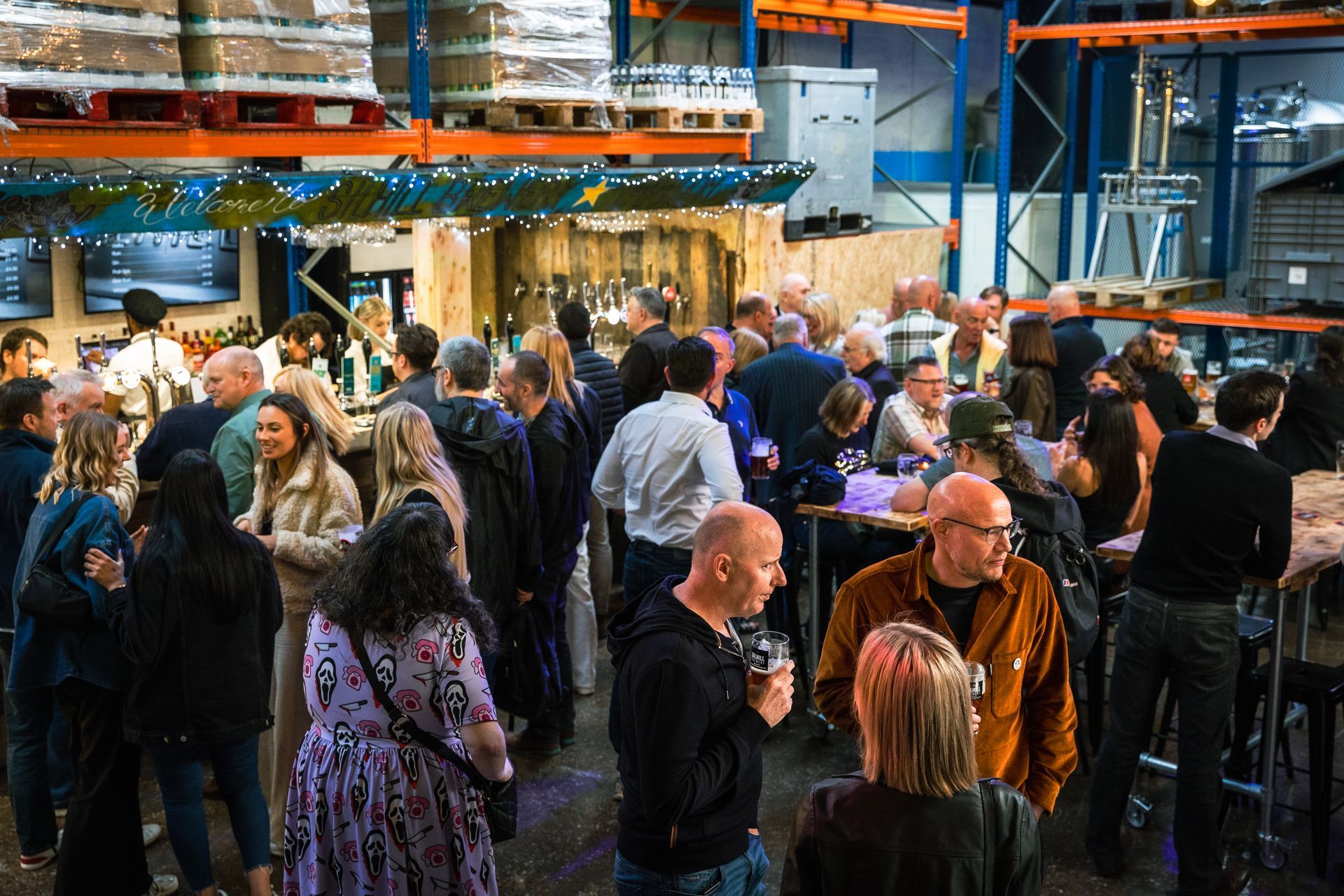 A large group of people are standing around tables in a warehouse.