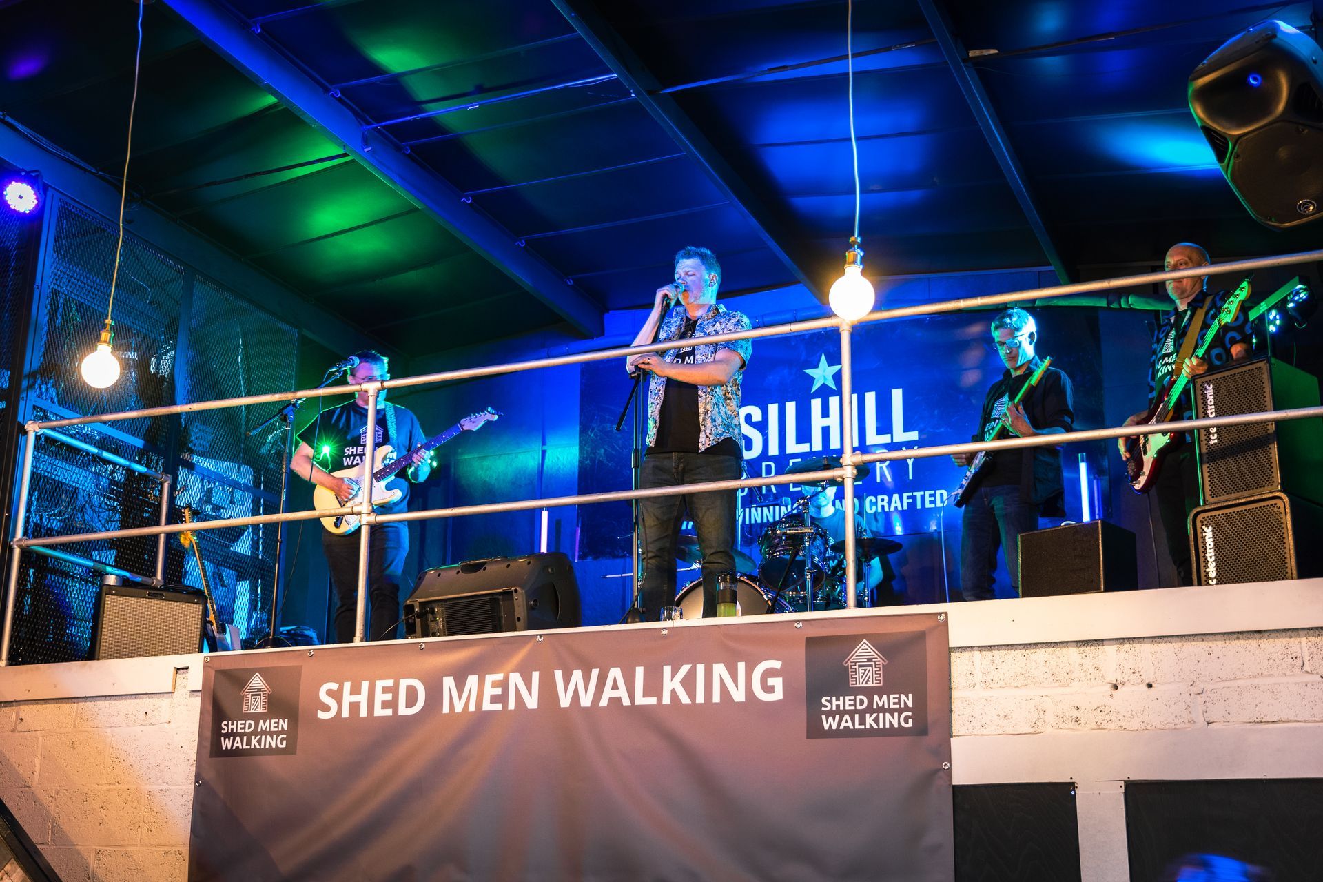 A group of men are on stage with a banner that says shed men walking