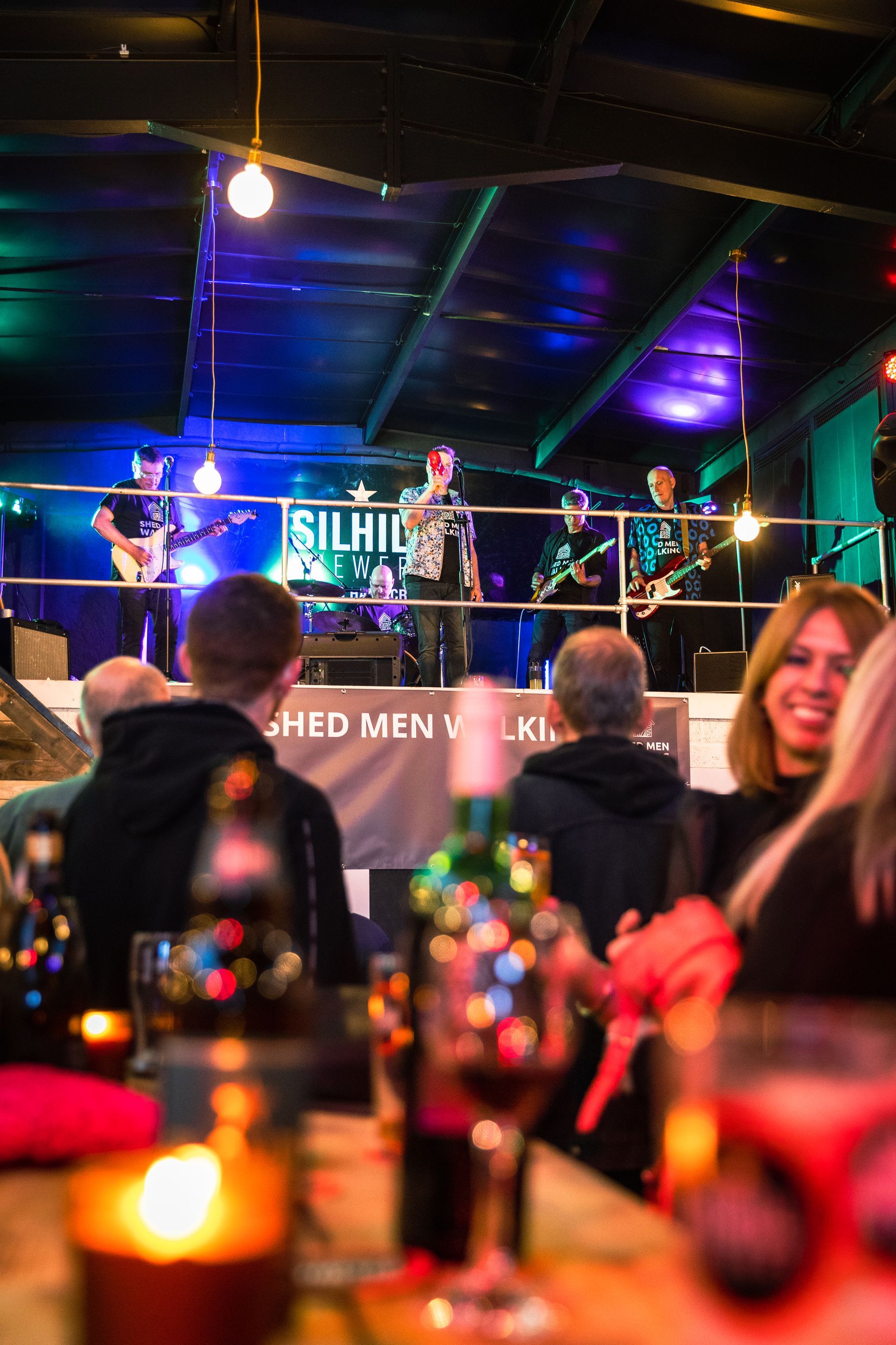 A group of people sitting at a table watching a band on stage