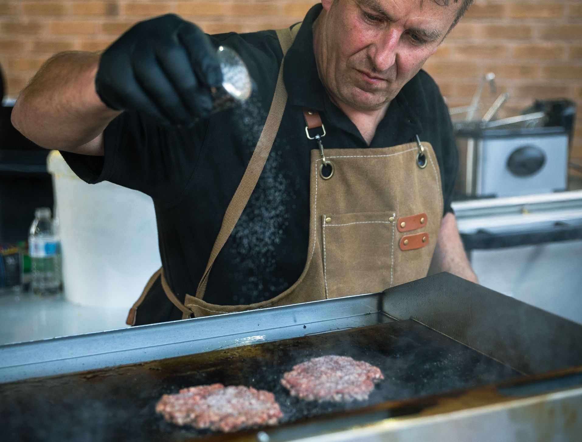 A man in an apron is cooking hamburgers on a grill.