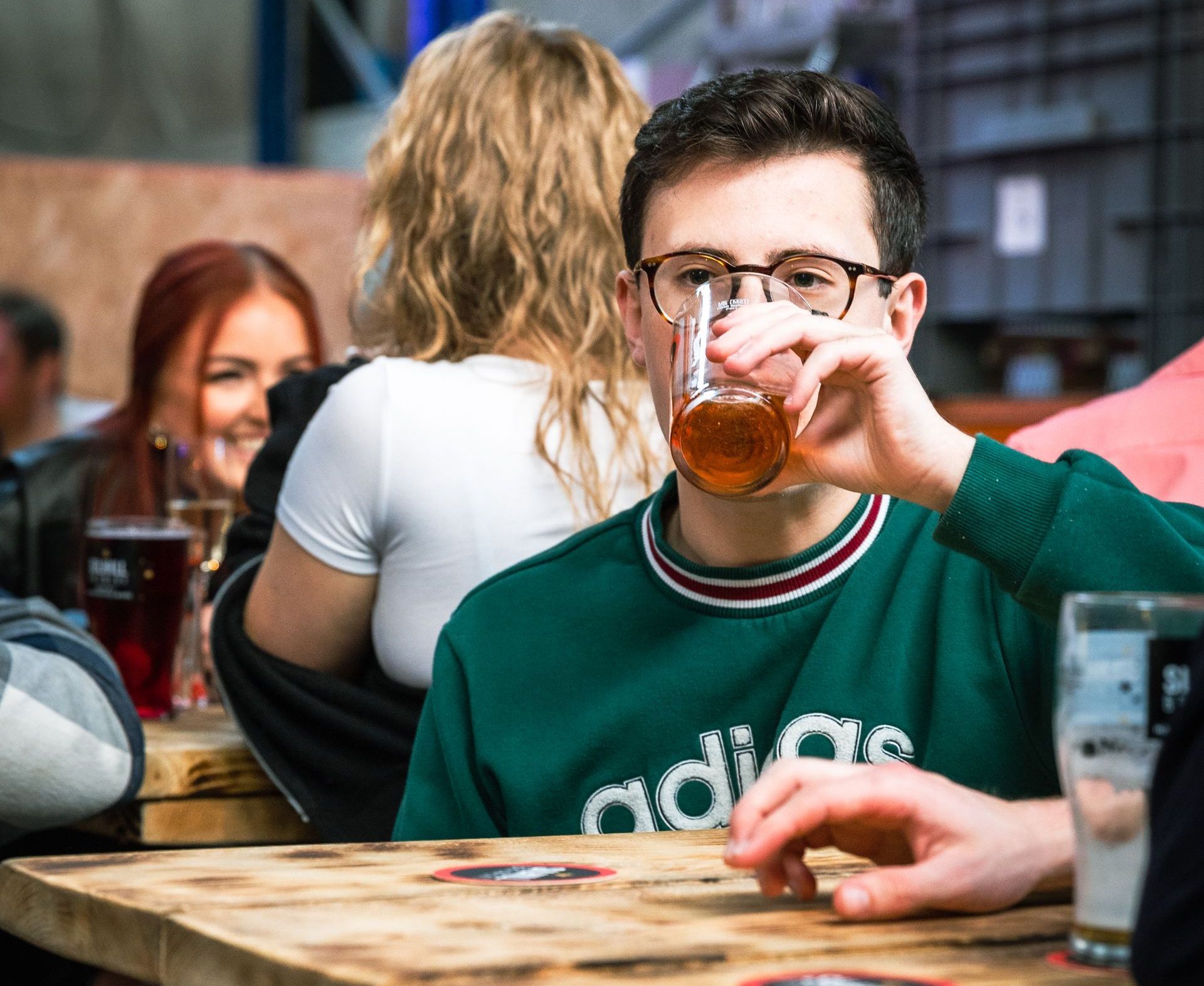 A man wearing glasses is sitting at a table drinking a beer.