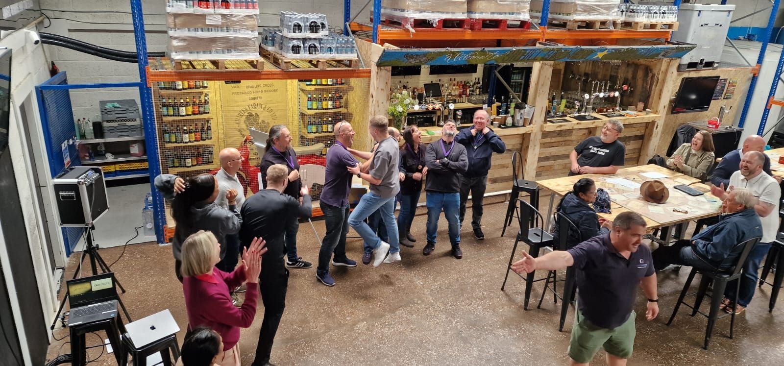 A group of people are dancing in a room with tables and chairs.