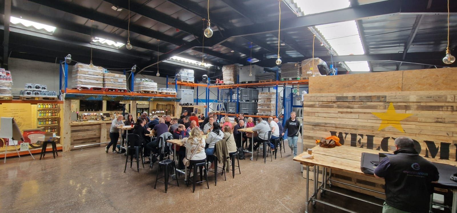 A group of people are sitting at tables in a warehouse.