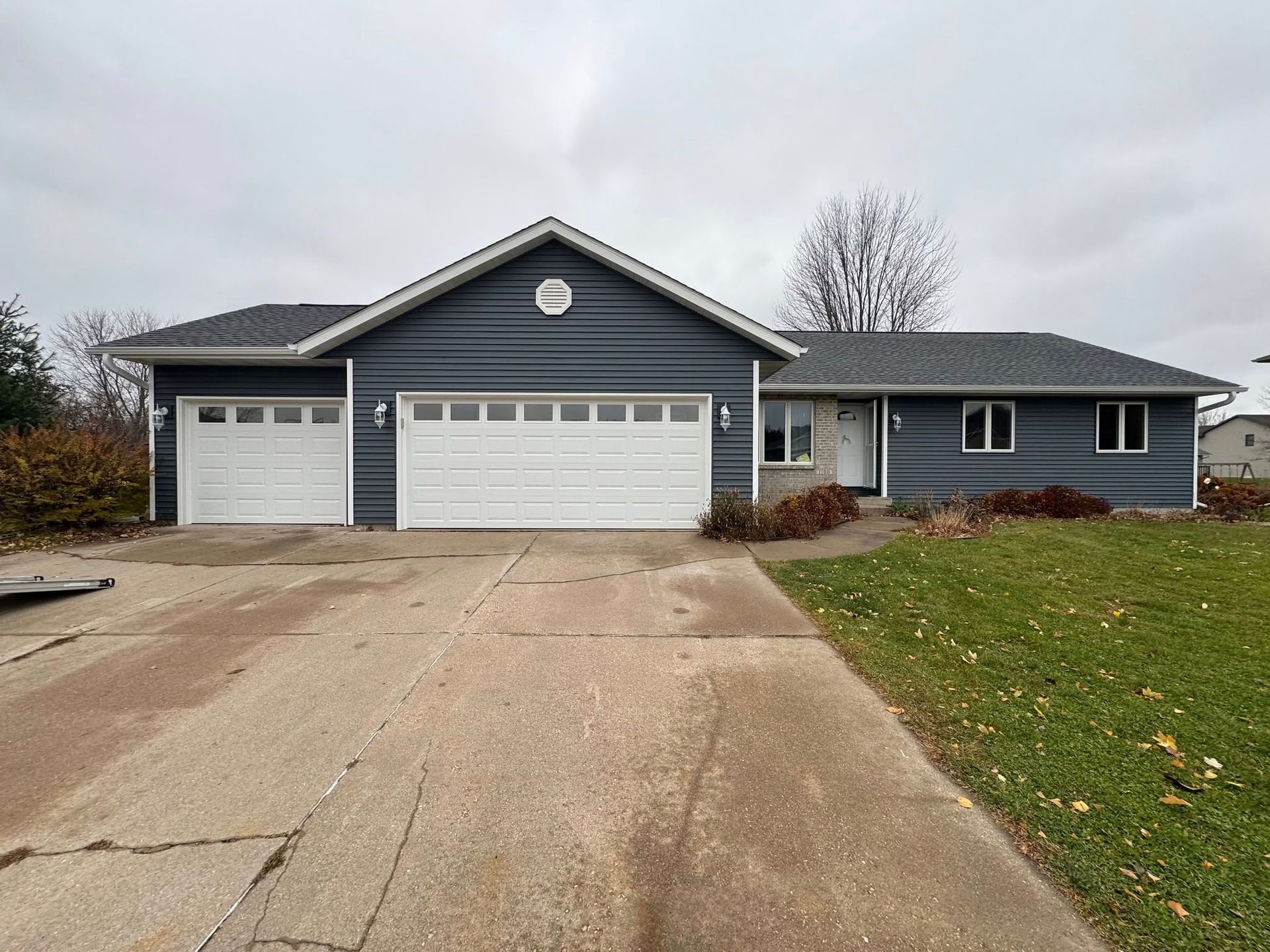 Suburban house with three-car garage, gray siding, and a concrete driveway under cloudy skies