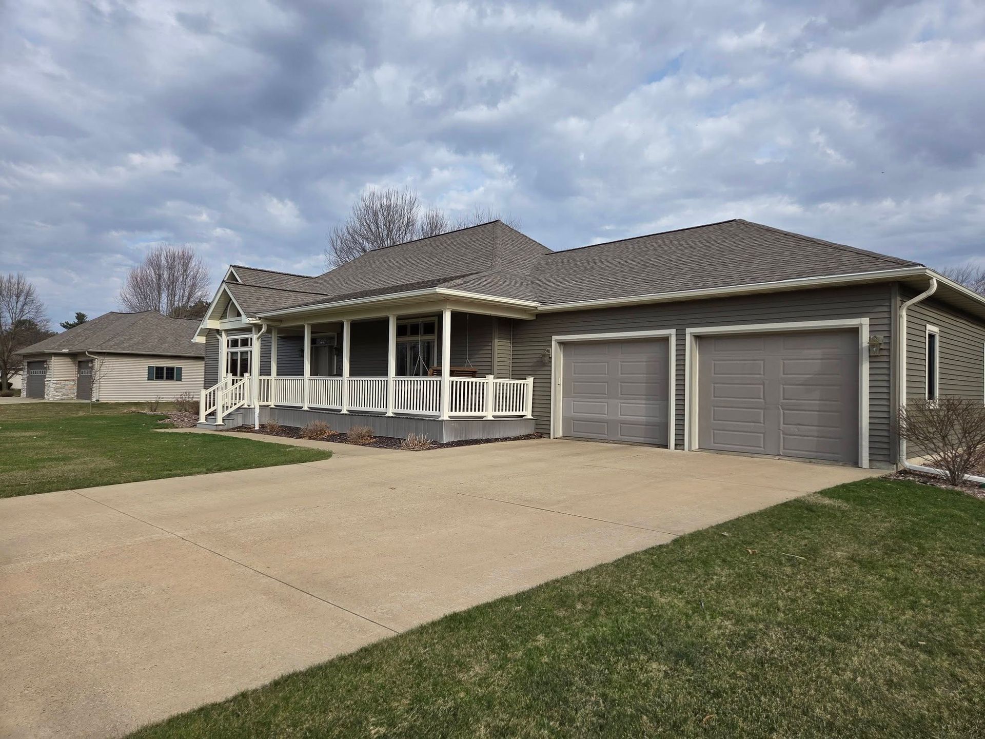 Suburban house with a front porch, double garage, and wide concrete driveway on a grassy lot