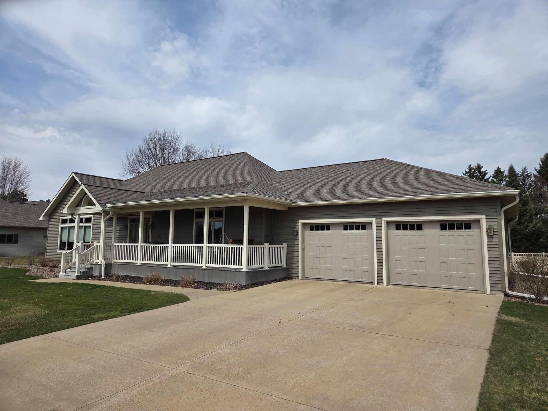 Suburban house with three-car garage, gray siding, and a concrete driveway under cloudy skies