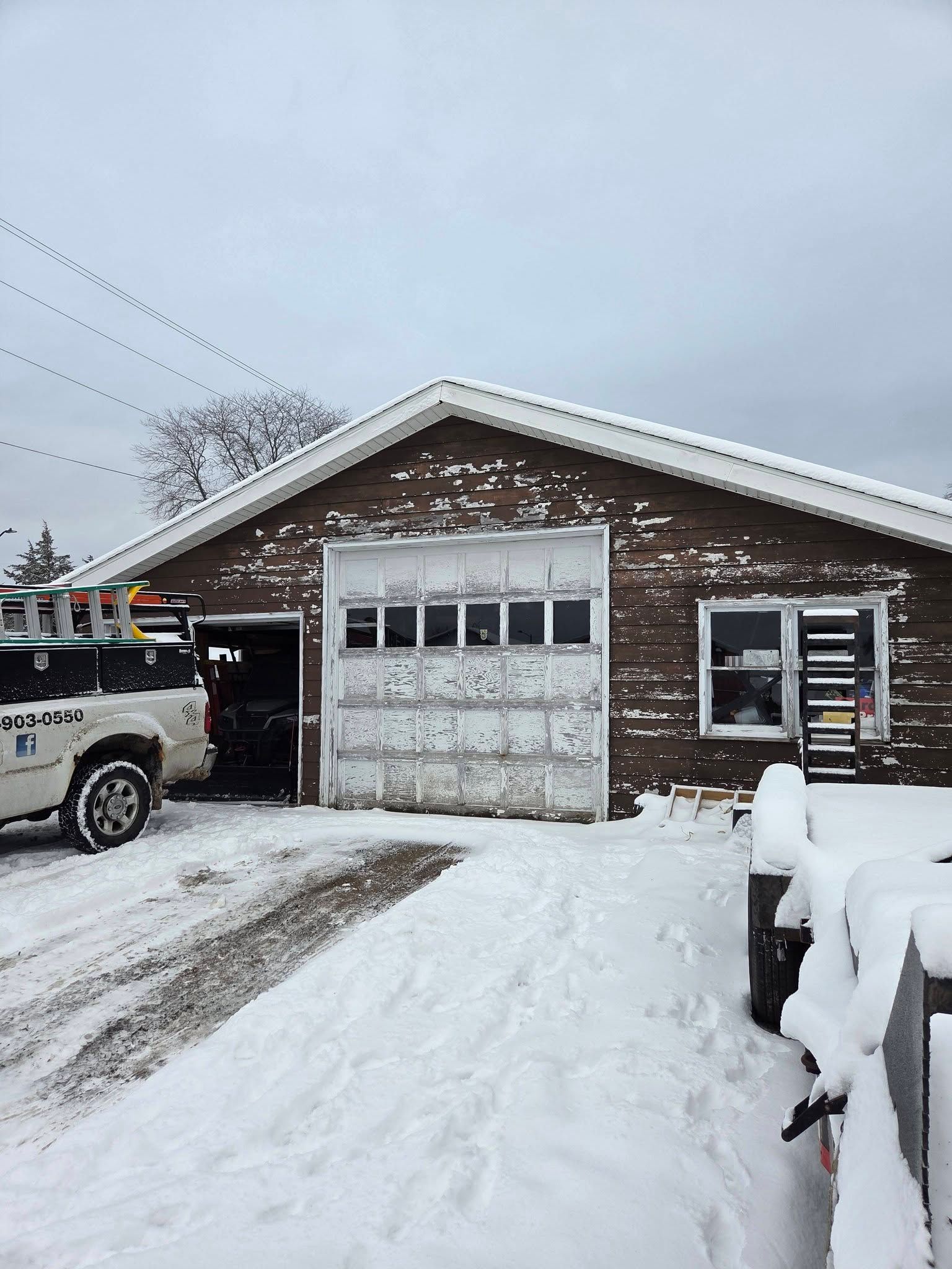 Snow-covered brick garage with a white truck parked beside it under an overcast sky