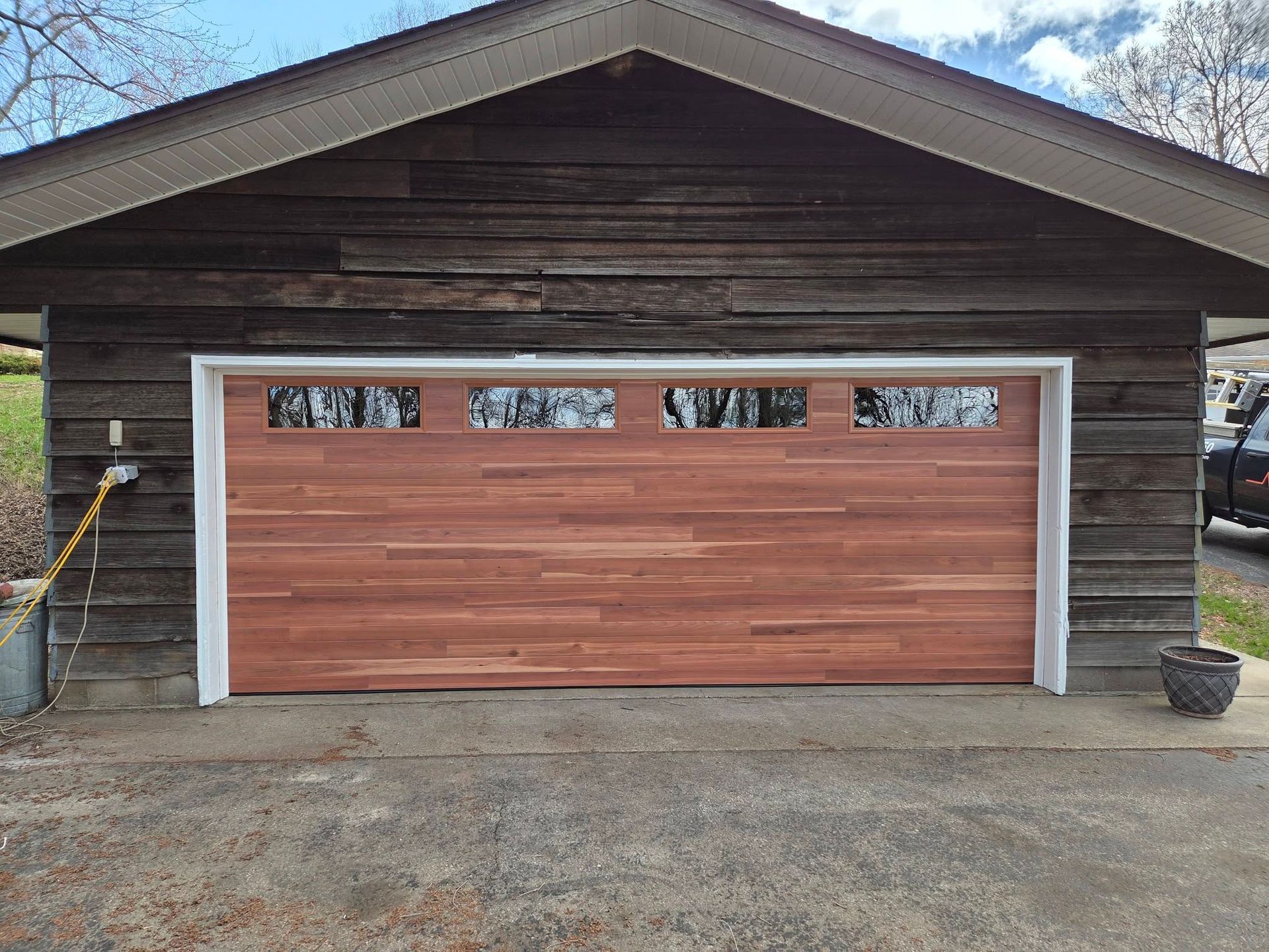 Wooden garage with a reddish-brown door and small upper windows, set beneath a gabled roof.
