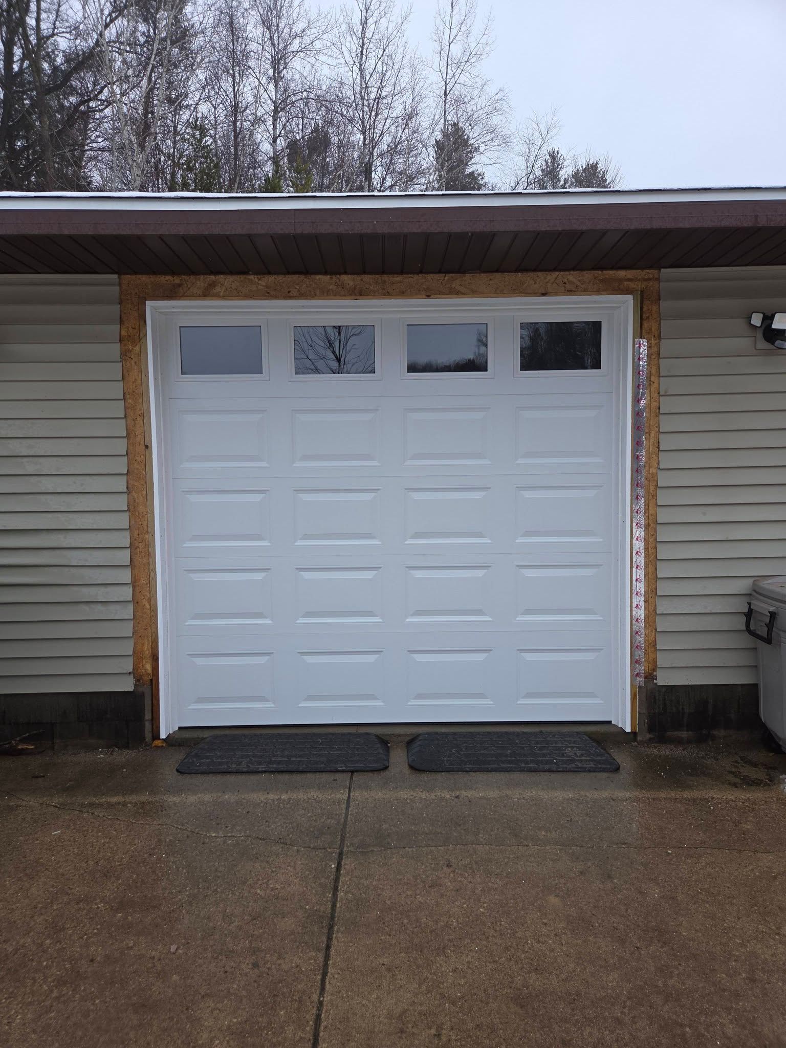 White garage door under a roof overhang with three small windows, viewed from a wet driveway