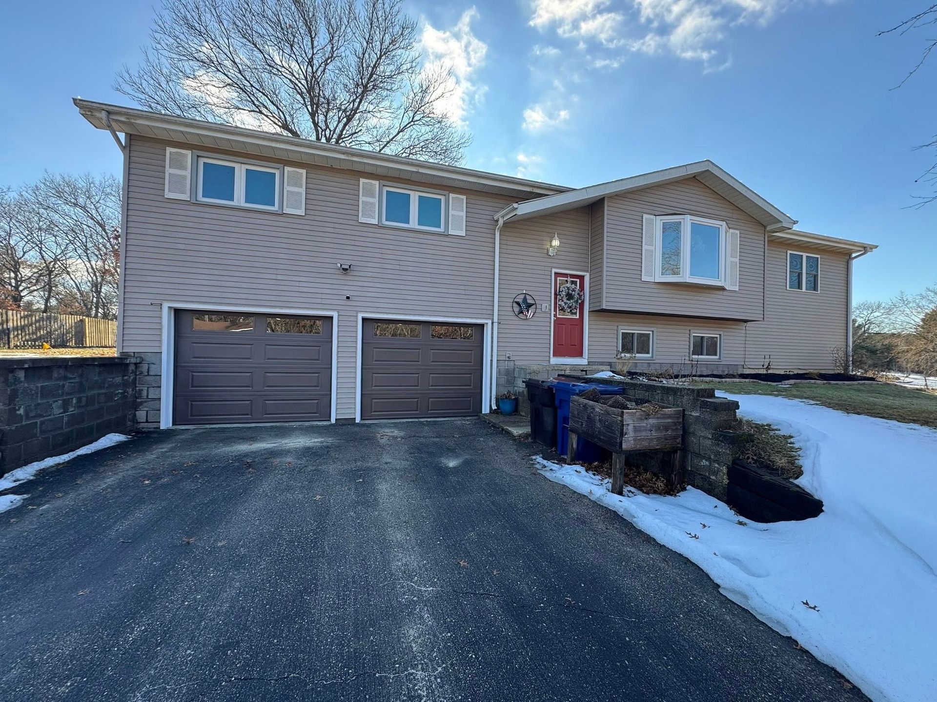 Suburban house with two garages, driveway, and snow along the front yard