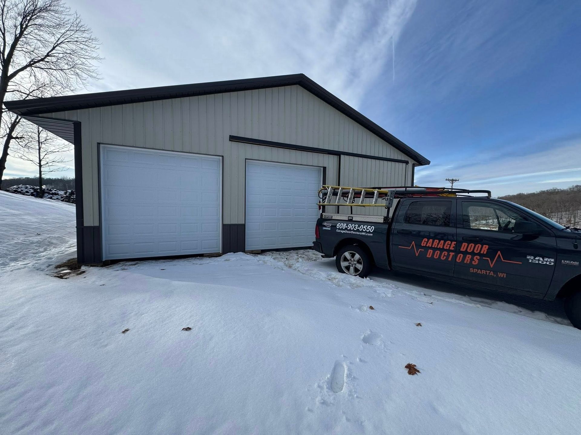 Snowy driveway with a metal garage and a black service truck parked beside it