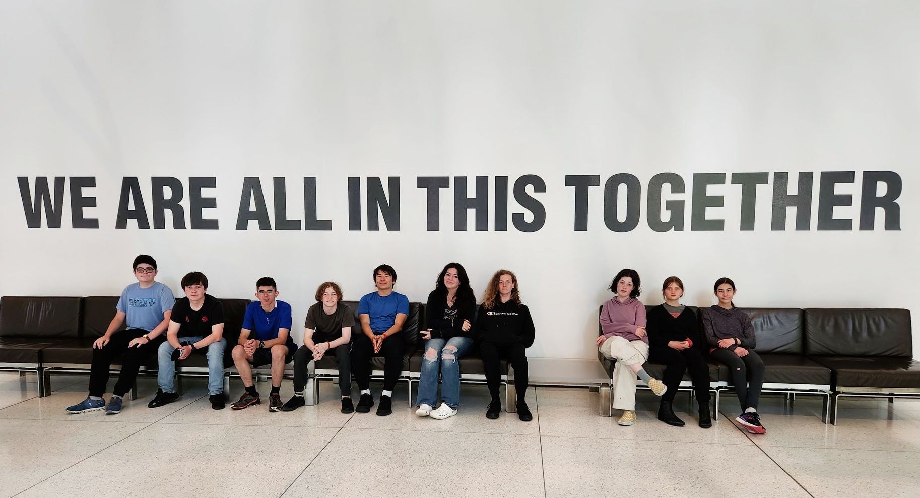 The Middle School class sitting in front of a museum mural that reads 