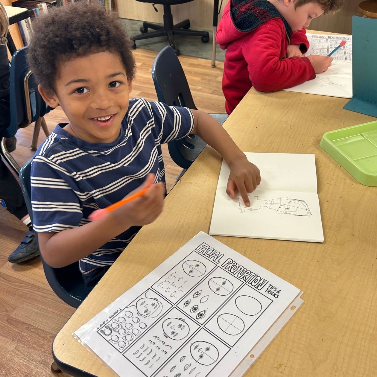 A Kindergarten Bridge student proudly shows off his drawing of his self-portrait.