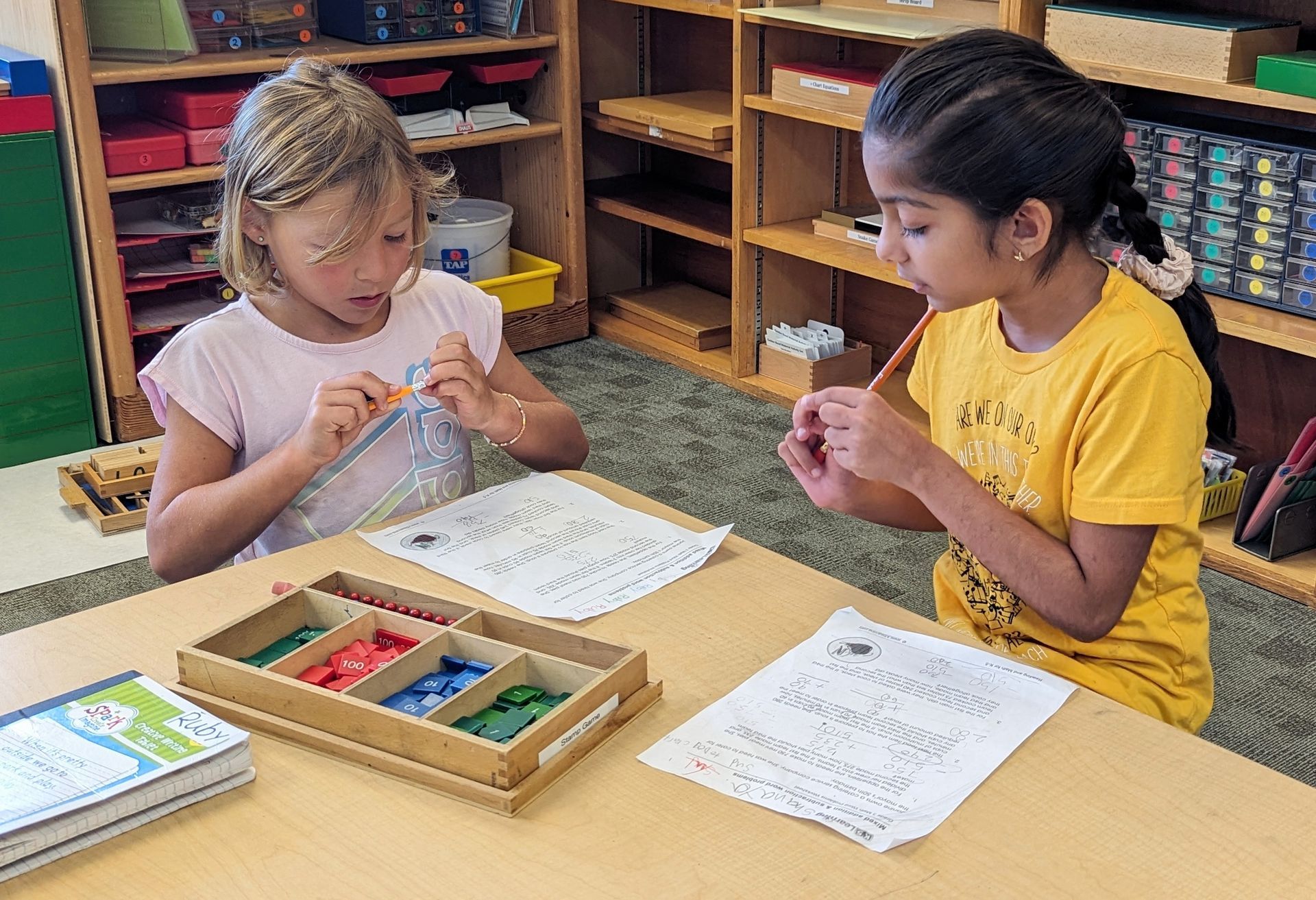 Two Lower Elementary students working on the Montessori Stamp Game (a math material). In the Montessori Elementary program at EBM.